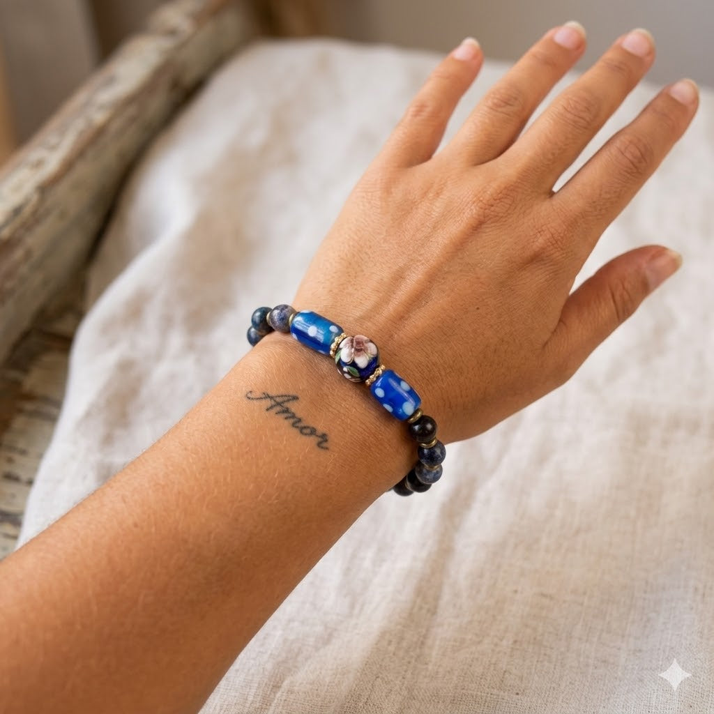 Hand wearing a beaded bracelet with blue and black beads on a neutral background